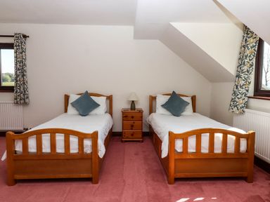 A bedroom with two single beds separated by a wooden nightstand and lamp at Valley House in Halberton near Tiverton
