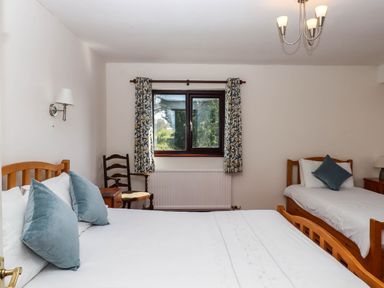 A bedroom with two wooden beds a window with patterned curtains and a wooden chair at Valley House in Halberton near Tiverton