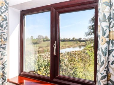 A view of a river and green fields through a wooden framed window with floral curtains at Valley House in Halberton near Tiverton