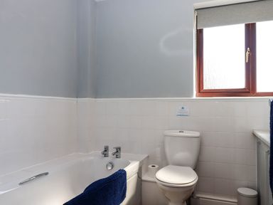 A bathroom with a bathtub a toilet a window and a blue towel at Valley House in Halberton near Tiverton