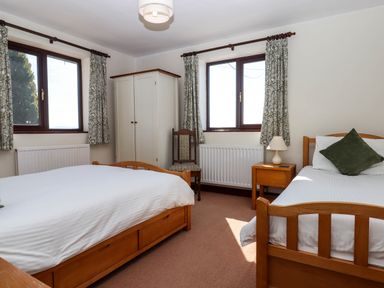 A bedroom with two single beds a wooden wardrobe a wooden chair and two windows at Valley House in Halberton near Tiverton