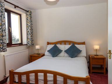 A bedroom with a wooden bed frame blue pillows bedside tables with lamps a window with patterned curtains and a radiator at Valley House in Halberton near Tiverton