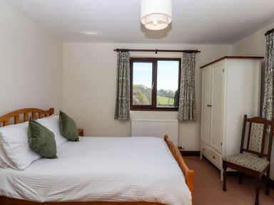 A bedroom with a wooden bed green cushions a white wardrobe and a patterned chair at Valley House in Halberton near Tiverton