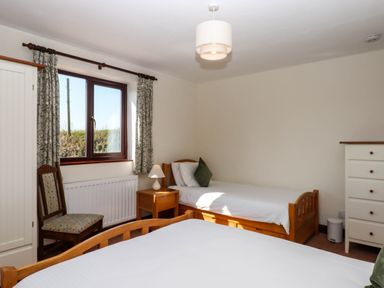A bedroom with two single beds a wooden chair a window with curtains a bedside table with a lamp and a white chest of drawers at Valley House in Halberton near Tiverton