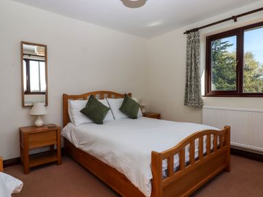 A bedroom with a wooden double bed green cushions bedside tables lamps window and a mirror at Valley House in Halberton near Tiverton