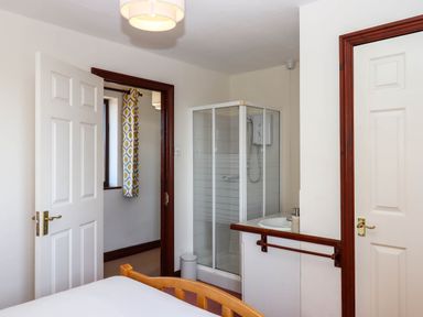 A bedroom with an adjacent bathroom featuring a shower cubicle a sink and two doors at Valley House in Halberton near Tiverton