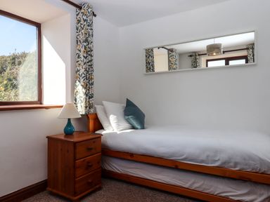 A bedroom with a single wooden bed white bedding a bedside table with a lamp and a window with floral curtains at Valley House in Halberton near Tiverton