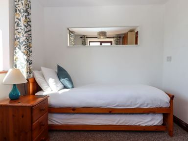 A bedroom with a wooden bed and white bedding next to a wooden nightstand with a lamp at Valley House in Halberton near Tiverton