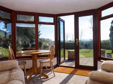 A sunroom with wooden table and chairs near glass doors opening to a garden at Valley House in Halberton near Tiverton