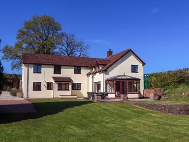 A large two story house with tiled roof and multiple windows with a lawn and patio area at Valley House in Halberton near Tiverton