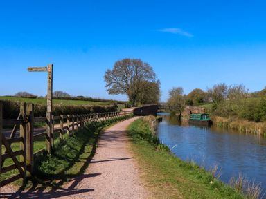 A canal with a narrowboat and a footpath with a wooden fence and a signpost near Valley House in Halberton near Tiverton