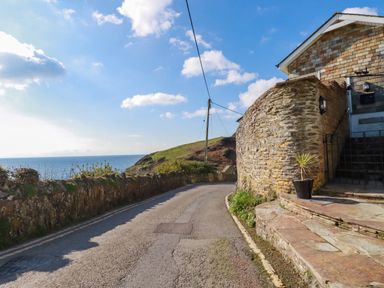 A coastal road with a stone wall and steps leading to a house at Suntrap House in Portloe