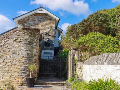 An entrance gate with stone walls and plants leading up to a house with a tiled exterior at Suntrap House in Portloe