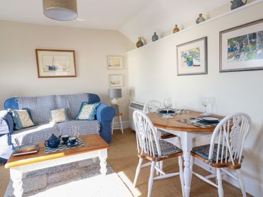 A living room with a blue sofa a wooden coffee table and a wooden dining table with white chairs at Suntrap House in Portloe