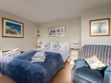 A bedroom with a double bed covered with a blue blanket and towels on it a blue armchair with a pillow and three framed pictures on the walls at Suntrap House Portloe