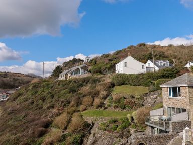 Houses on a hillside with stone walls and greenery under a blue sky at Suntrap House in Portloe