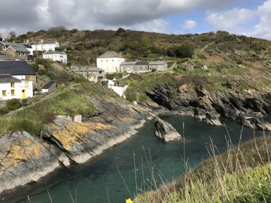 A coastal village with houses on rocky cliffs above clear water at Suntrap House in Portloe