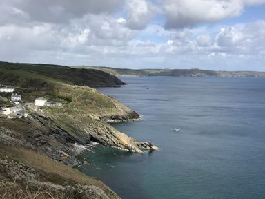 A coastal landscape with cliffs houses and a boat on the sea at Suntrap House in Portloe