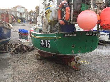 A dock area with a green fishing boat named Jasmine Falmouth on dry land near stacked crates and buildings
