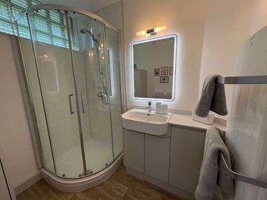 A bathroom with a glass shower enclosure a sink with cabinet a lighted mirror and towels on a radiator at Suntrap House in Portloe