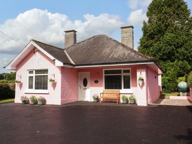 A pink house with a porch and a bench at Rosemont in Adare