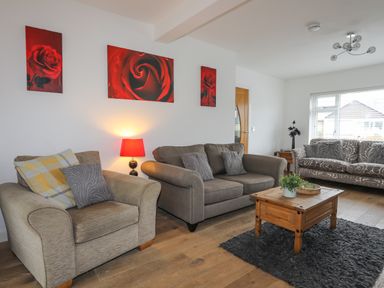 A living room with three sofas a coffee table a lamp and red rose paintings on the wall at Monarfon in Criccieth