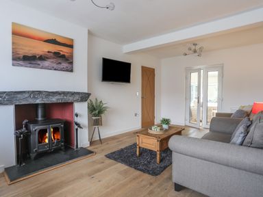 A living room with a wood burning stove a gray sofa a wooden coffee table and a wall mounted television at Monarfon in Criccieth