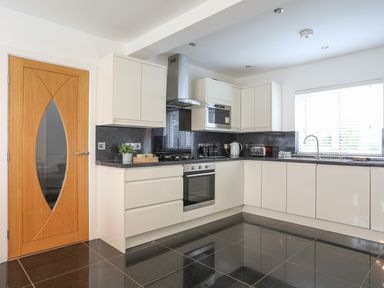 A kitchen with white cabinets black countertops stainless steel oven and stove a wooden door and a window with blinds at Monarfon in Criccieth