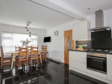 A kitchen with a dining table and chairs next to a window and modern cabinetry and appliances at Monarfon in Criccieth