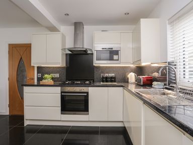 A modern kitchen with white cabinets black countertops stainless steel oven and gas stove with a sink and window blinds at Monarfon in Criccieth