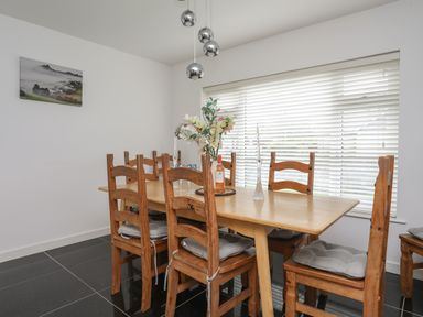 A dining room with a wooden table and chairs cushions flowers and a bottle on the table at Monarfon in Criccieth
