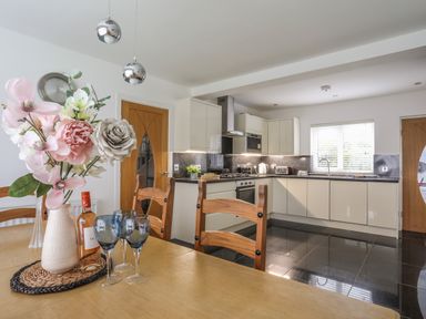 A kitchen with wooden chairs and a table with flowers and wine glasses at Monarfon in Criccieth