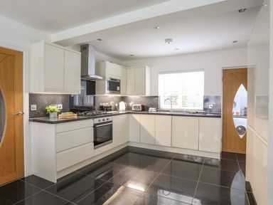 A kitchen with white cabinets black countertops and tiled floor at Monarfon in Criccieth