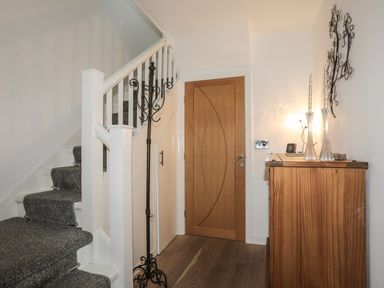 A hallway with carpeted stairs a wooden door a coat rack and a wooden cabinet with decorative items at Monarfon in Criccieth