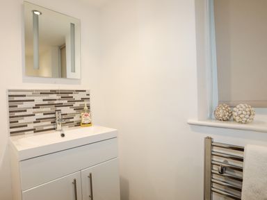 A bathroom with a white sink cabinet a rectangular mirror and a tiled backsplash at Monarfon in Criccieth