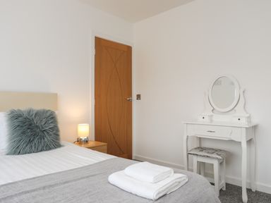A bedroom with a bed a bedside table with lamp a wooden door and a white dressing table with stool at Monarfon in Criccieth