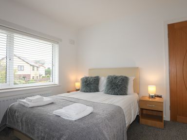 A bedroom with a bed with grey throw and two bedside tables with lamps at Monarfon in Criccieth