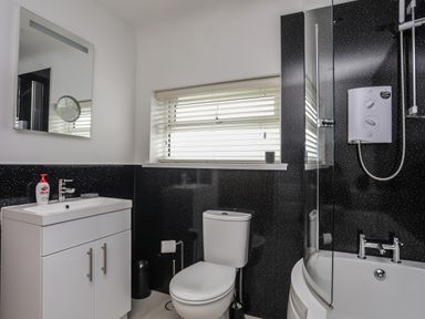 A bathroom with a white sink cabinet mirror toilet bathtub shower and window blinds at Monarfon in Criccieth