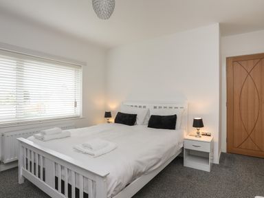 A bedroom with a white bed frame two black pillows white bedside tables with lamps and a wooden door at Monarfon in Criccieth