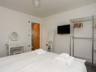 A bedroom with a white bed with folded towels a white dressing table with a stool a full-length mirror a wall-mounted TV and a metal clothes rack at Monarfon in Criccieth