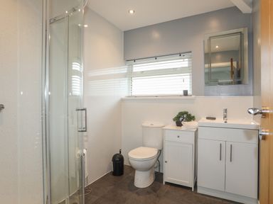 A bathroom with a shower cubicle a toilet a white cabinet a sink with vanity and a window with blinds at Monarfon in Criccieth