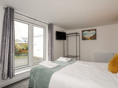 A bedroom with a bed folded towels a wall-mounted TV glass doors with curtains and a clothes rack at Monarfon in Criccieth