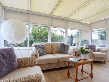 A sunroom with wicker sofas with cushions and a wooden coffee table with a plant at Monarfon in Criccieth