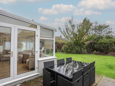 A garden with a black outdoor dining table and chairs next to a conservatory at Monarfon in Criccieth