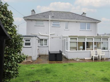 The back exterior of a two story house with a patio seating area and green lawn at Monarfon in Criccieth
