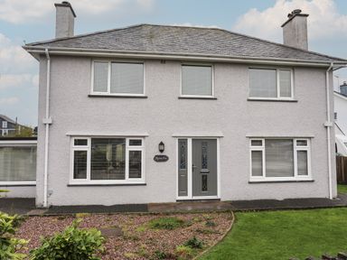 A two-story house with gray exterior walls white window frames and a gray front door with garden in front at Monarfon in Criccieth