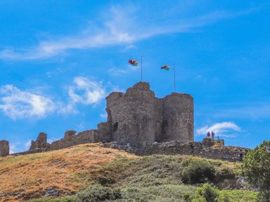 Old stone castle ruins on a hill with two flags flying at Monarfon in Criccieth