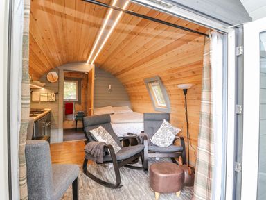A small wooden pod interior with two gray rocking chairs, a bed, a kitchen area, and a floor lamp at Elleric Pods - The Last Resort Fasnacloich near Appin