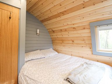 A bedroom with a double bed a wooden door and a window in a wooden pod at Elleric Pods - The Last Resort in Fasnacloich near Appin