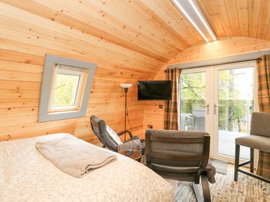 A wooden interior room with a bed a chair a floor lamp a wall-mounted TV and glass doors at Elleric Pods - The Last Resort Fasnacloich near Appin